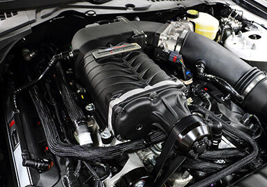 Close-up view of a car engine featuring a Roush Mustang Supercharger with advanced TVS Technology. The engine, boasting Phase 2 727 HP, is mounted in a well-organized compartment with all surrounding components clearly visible.
