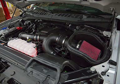 Close-up of an open car hood showcasing the engine components, including a Roush Cold Air Intake Kit with a red air filter, a coolant reservoir, and various pipes and wires of the high-performance F-150 EcoBoost.