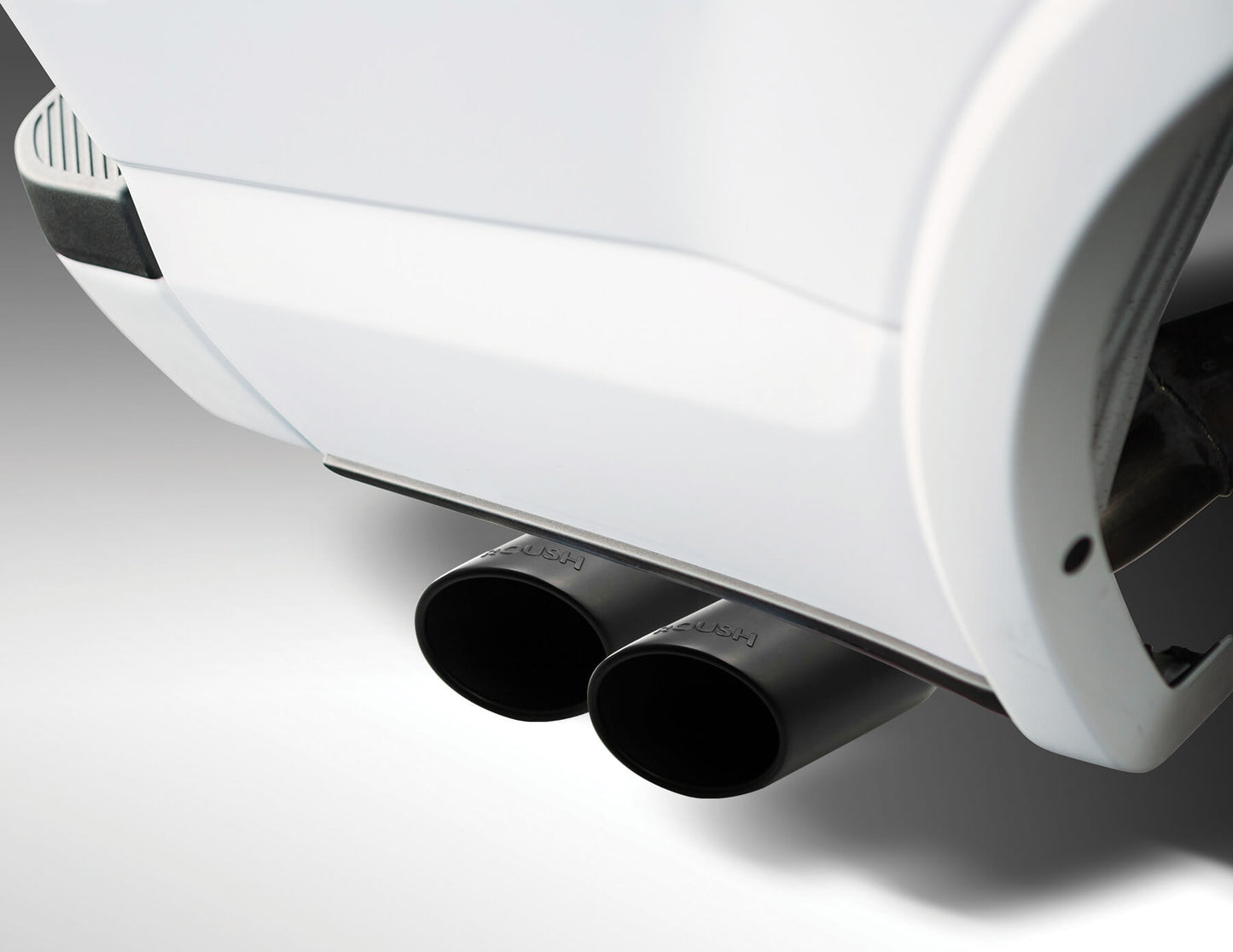 Close-up of a car's dual black exhaust pipes from a Roush F-150 cat back exhaust, extending from a white vehicle against a neutral background.